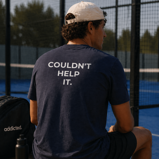 Person sitting on a bench with 'Couldn't Help It.' shirt on a tennis court