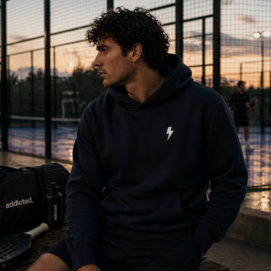 Man wearing a black hoodie with a logo sitting on a court at sunset.