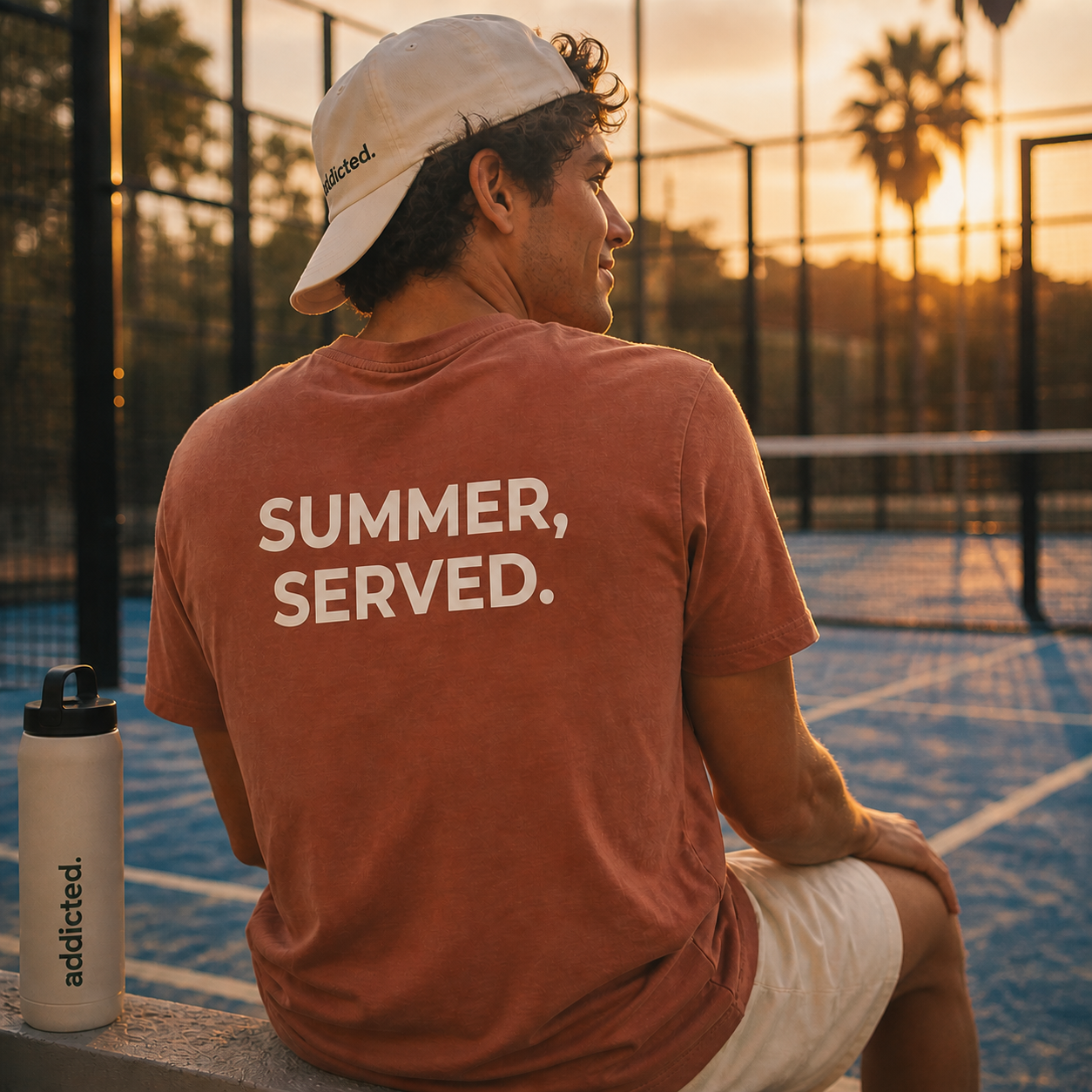 Person wearing a 'Summer, Served.' t-shirt on a padel court at sunset