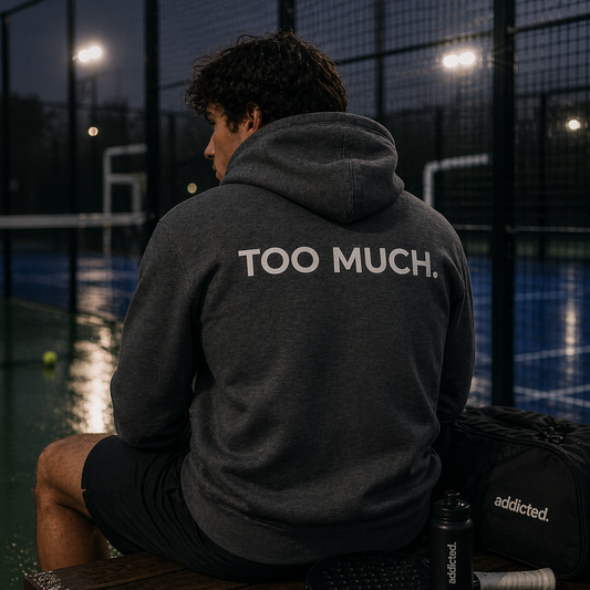 Person wearing a hoodie with 'Too Much' text on a dark outdoor court.