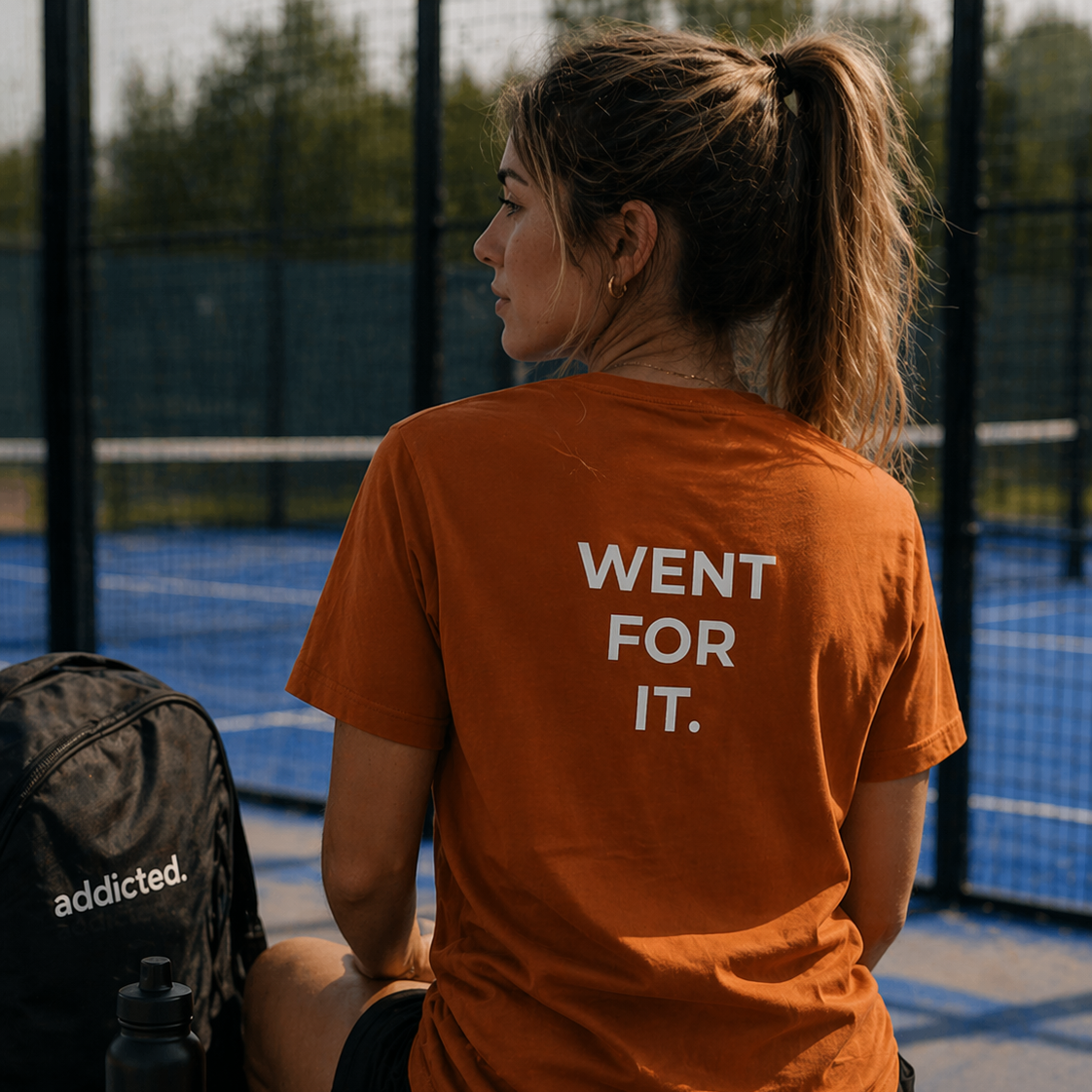Person wearing an orange t-shirt with 'Went for it.' on a padel court