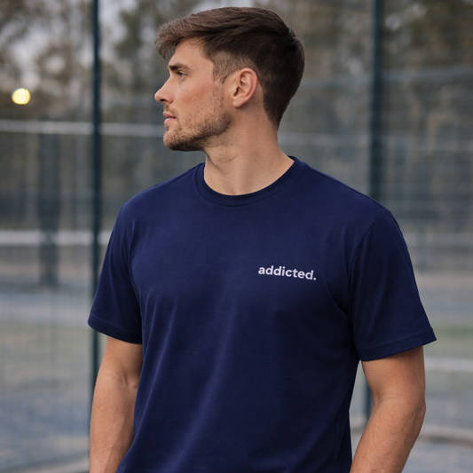 Man wearing a navy blue t-shirt with 'addicted.' text on an outdoor court.