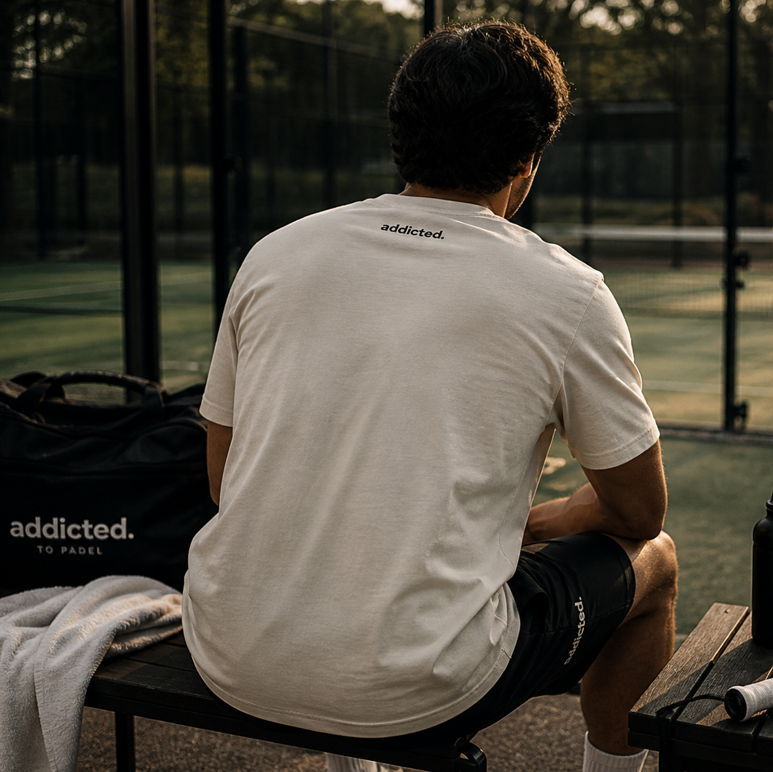 Person sitting on a bench with 'addicted' t-shirt at a padel court