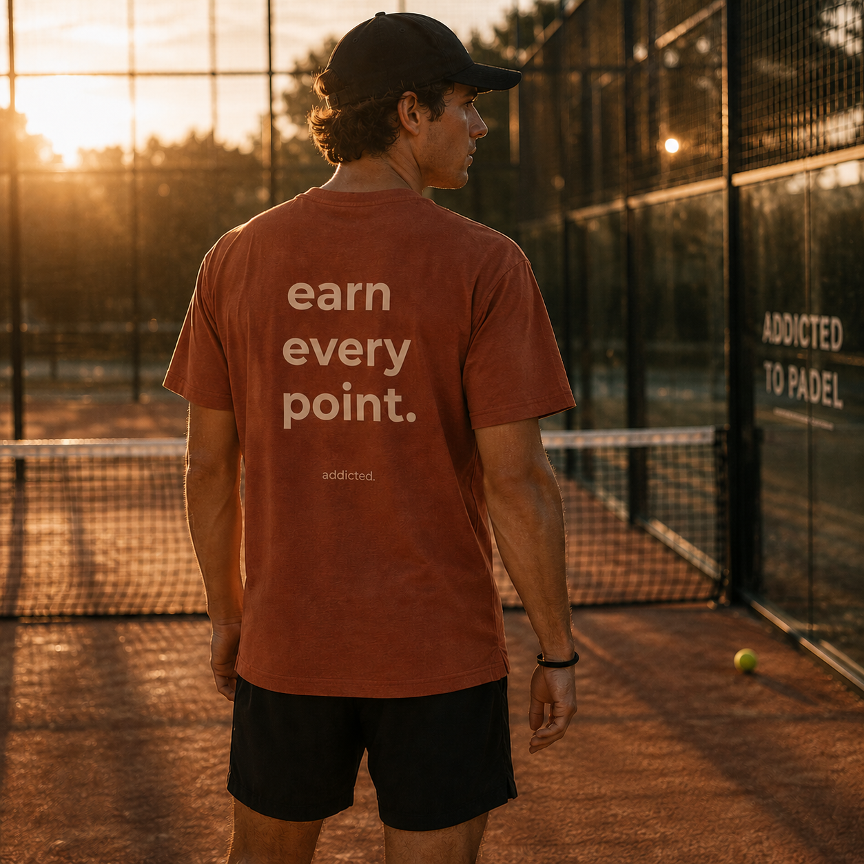 Person wearing a t-shirt with 'earn every point' on a tennis court at sunset.