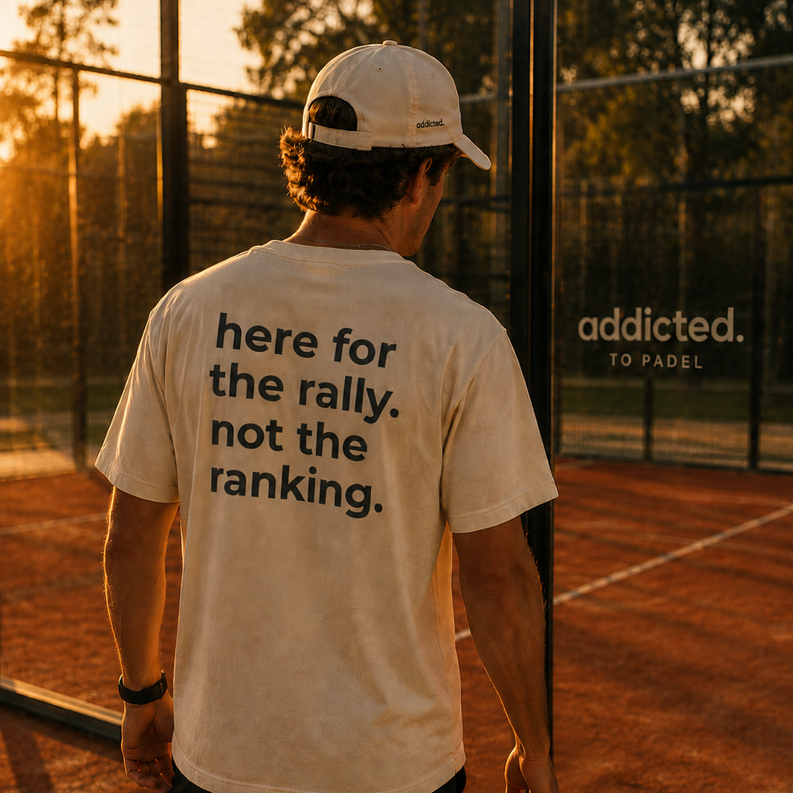 Person on a padel court wearing a t-shirt with a message, standing in front of a 'addicted to padel' sign.