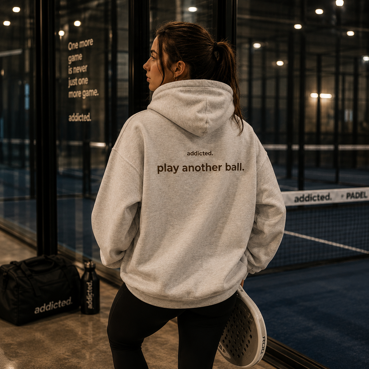 Person wearing a hoodie with 'addicted. play another ball.' text in an indoor sports facility.