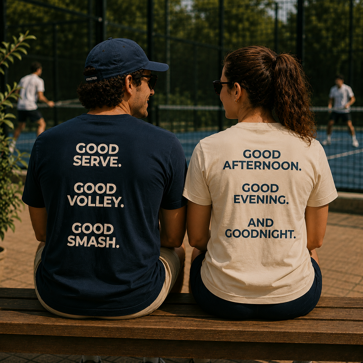 Two people sitting on a bench at a tennis court, wearing t-shirts with tennis-themed text.